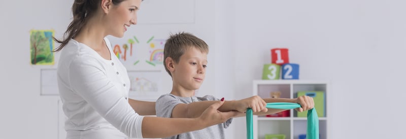 Female therapist showing young boy how to properly hold a rubber band during exercises
